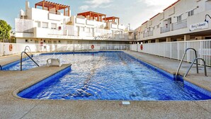 A swimming pool with a clear blue water, surrounded by a white building with balconies and a covered area.