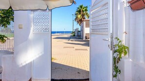 A doorway leading to a beachside area with a clear view of the sea, a palm tree, and a tiled walkway.