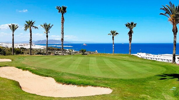 A golf course with a clear view of the ocean and a city in the distance.