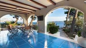 A covered patio with a blue-tiled floor, a table with chairs, and a view of the sea and mountains. - Beachfront Villa Zara  (Mimice)
