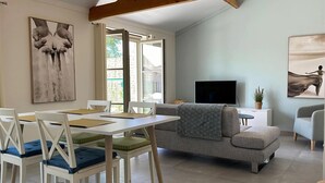 Un salon spacieux comprenant un coin repas, un canapé, un téléviseur et des œuvres d’art accrochées aux murs.