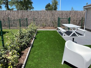 A patio area with a white table and benches, surrounded by a low stone wall and green plants. - Holiday Home in Koksijde Near Sint-andre Beach (Koksijde)