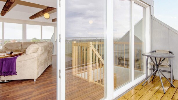 A balcony with a wooden deck, a sofa, and a table. - 6 Person Holiday Home in Harboore (Harboore)