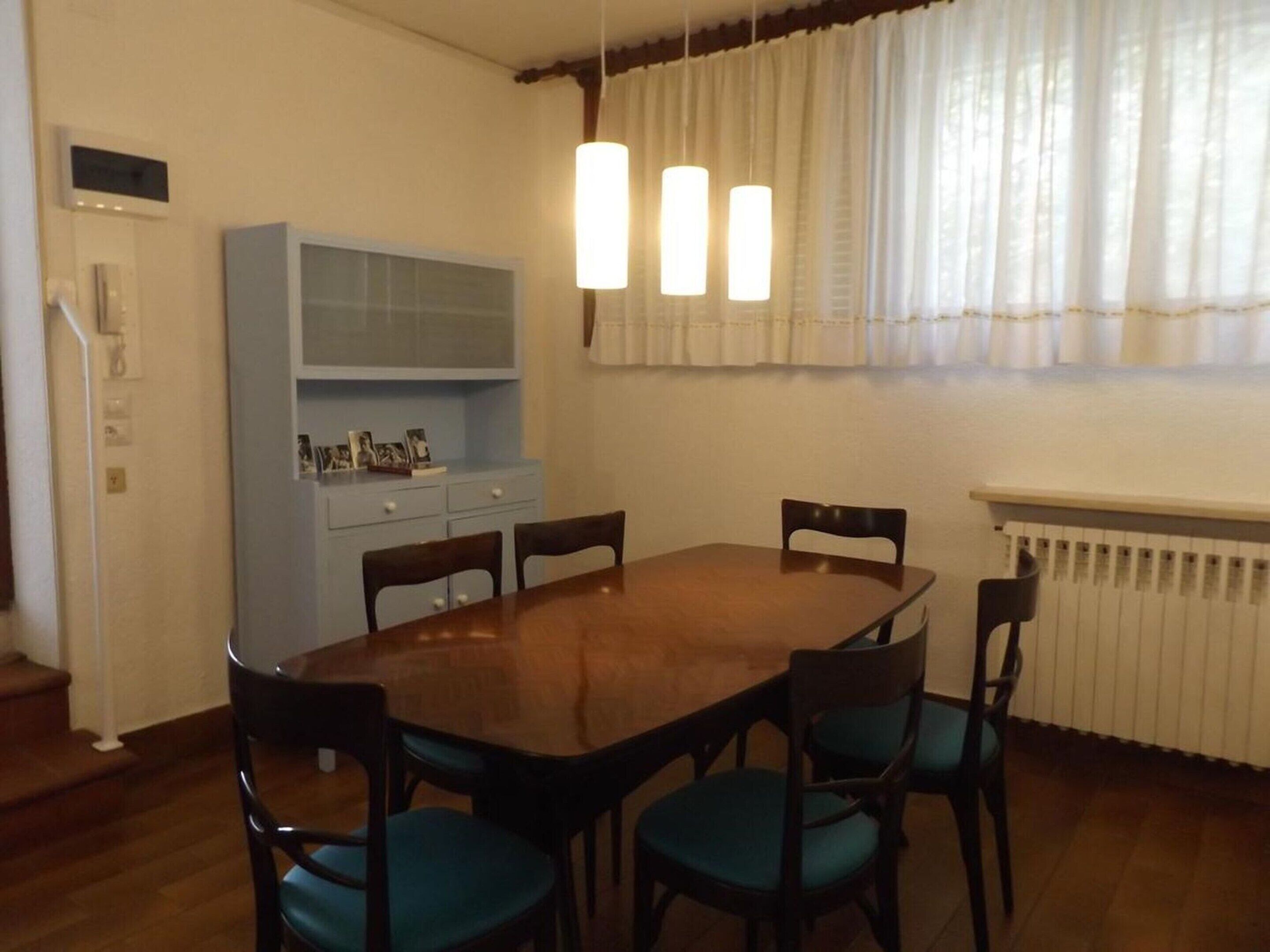 A dining room with a wooden table and chairs, a blue cabinet, and a window with curtains.