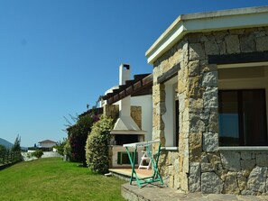 A stone house with a chimney, a small porch, and a grassy yard. - Villa in Alghero With Pool & Near Town (Alghero)