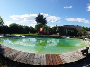 A swimming pool with a wooden deck, surrounded by trees and a small building. - Haus Sommerwind OG Comfortable Vacation Home (Klink)
