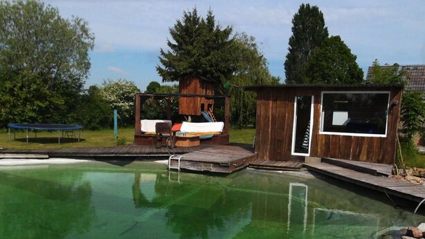 Une piscine avec une terrasse en bois, un petit chalet en bois et un espace détente doté d’un toboggan.