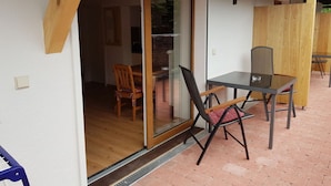 A patio with a glass door leading to an interior space, a table with chairs, and a wooden fence. - am Buchbrunnen Comfortable Holiday Residence (Pfronten)