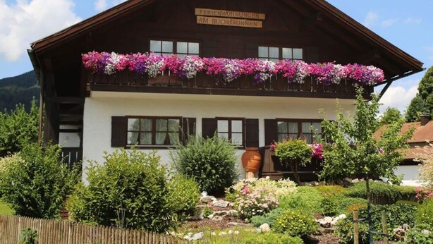 A traditional chalet with a balcony adorned with flowers, surrounded by lush gardens. - am Buchbrunnen Comfortable Holiday Residence (Pfronten)