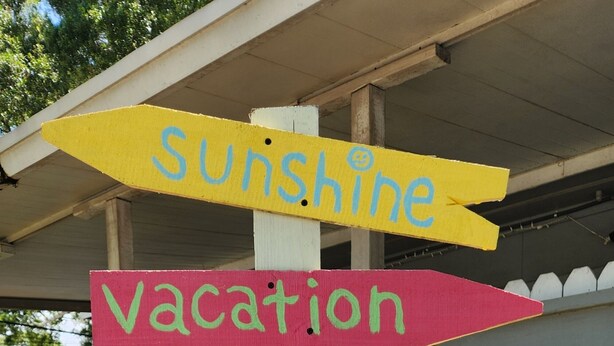A wooden signpost with multiple directional arrows pointing to various destinations such as Sunshine, Vacation, Beaches, Studio 924, Squirrels, Relax, and Happiness. - Quaint studio (Largo)