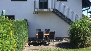 A two-story building with a balcony, a staircase, and a patio area with a table and chairs. - Inviting Apartment in Pruchten With Garden (Pruchten)