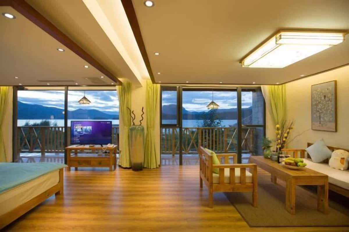 Um quarto amplo com piso de madeira, uma cama, uma TV, uma mesa de jantar e um sofá.