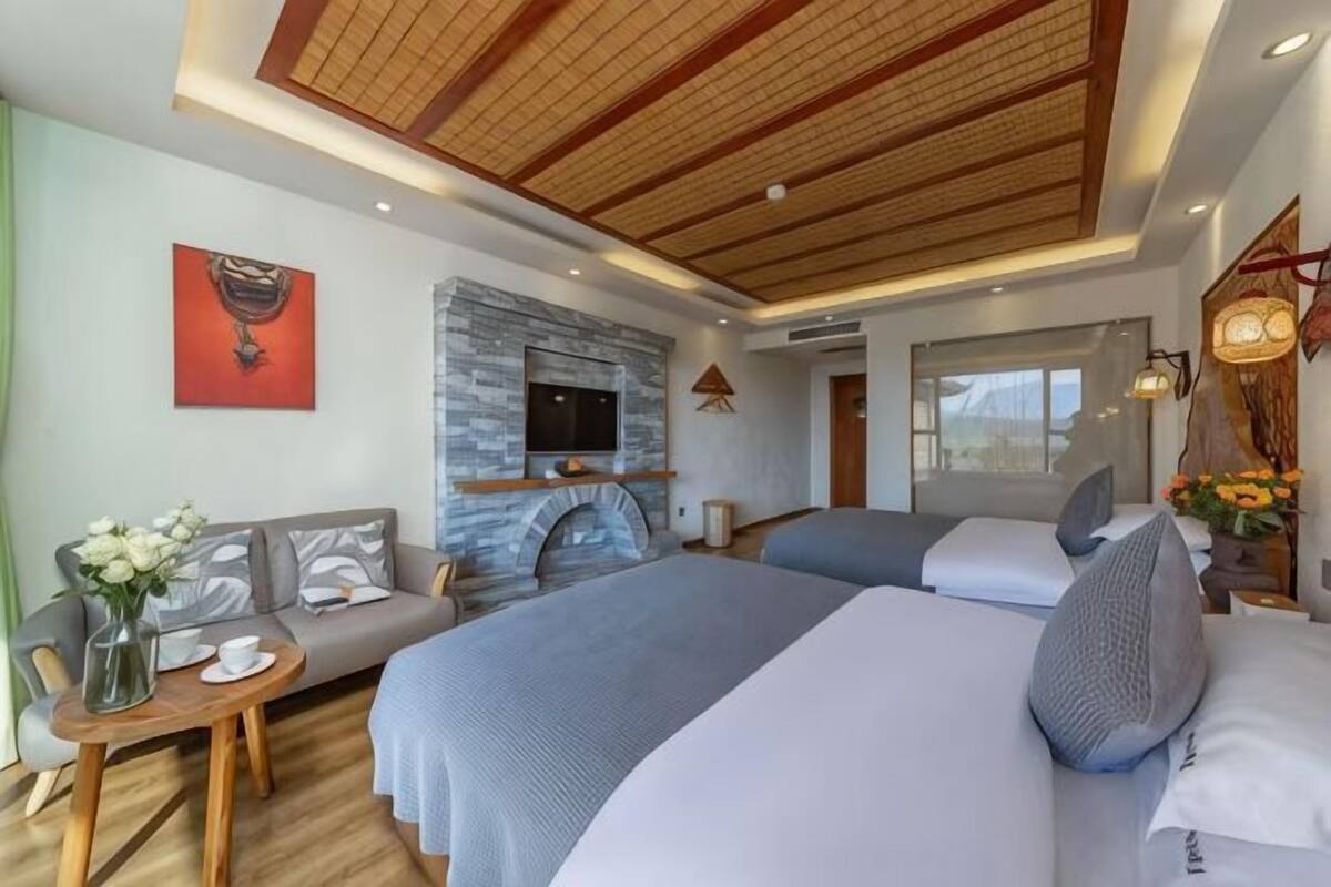 Quarto de hotel com lareira, duas camas, um sofá, uma TV e vista para a cidade.