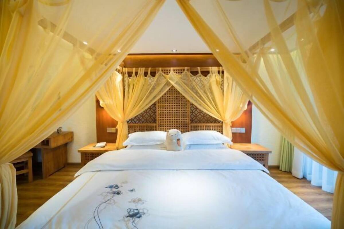 Quarto com cama de dossel, cabeceira de madeira, mesas de cabeceira e mesa de apoio.