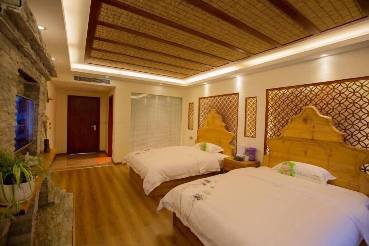 Quarto de hotel com duas camas, parede de pedra, teto de madeira e cabeceira decorativa.