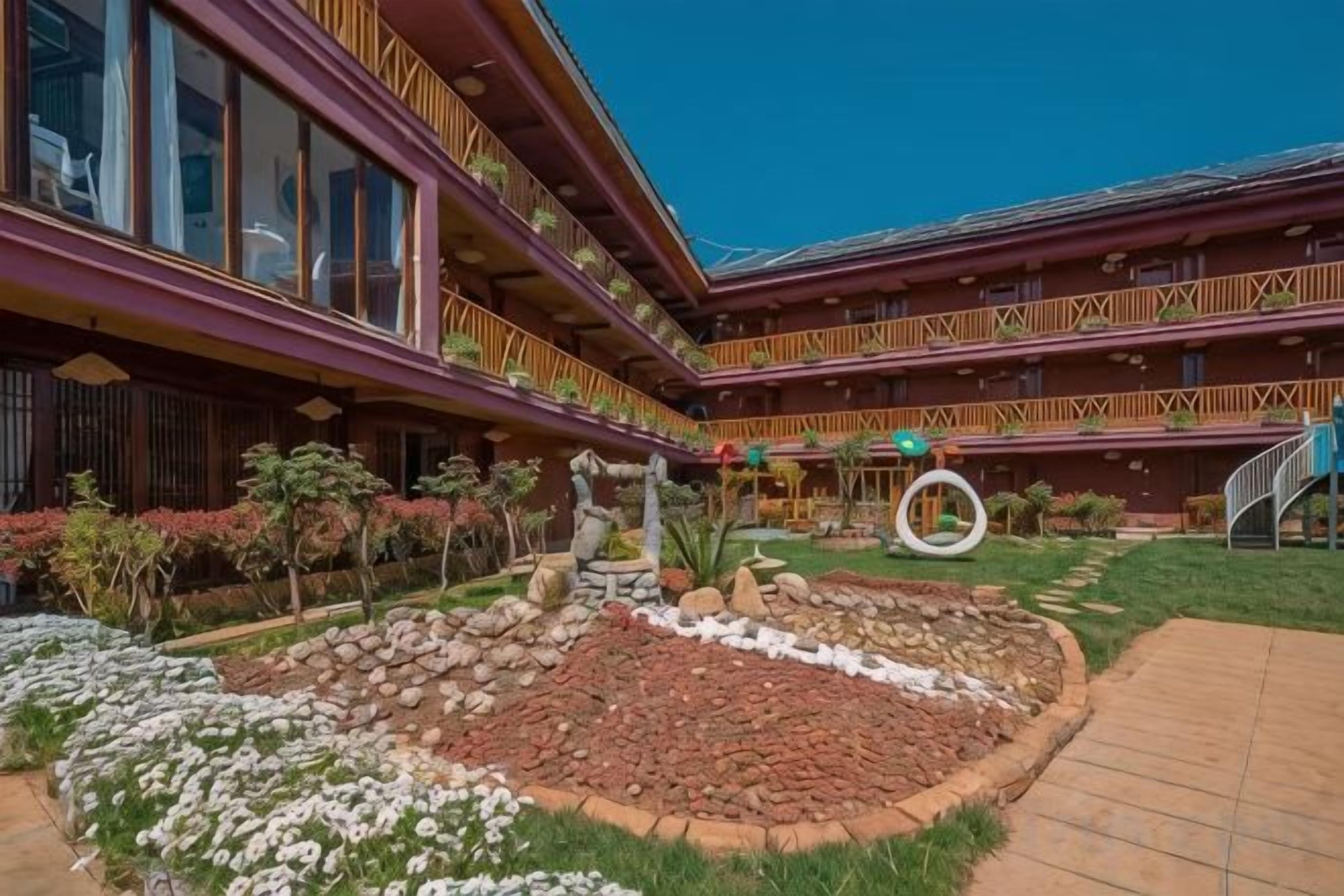 Un hotel con varios balcones, un patio central con un jardín circular y un cielo despejado.