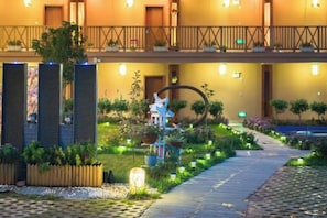A hotel entrance with a pathway leading to the main building, a small garden area with plants and a decorative structure, and a balcony with railings. - YingHuoChong (Ninglang)