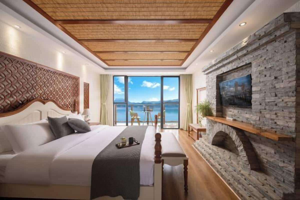 Quarto com uma cama grande, lareira de pedra, televisão e vista para o mar.
