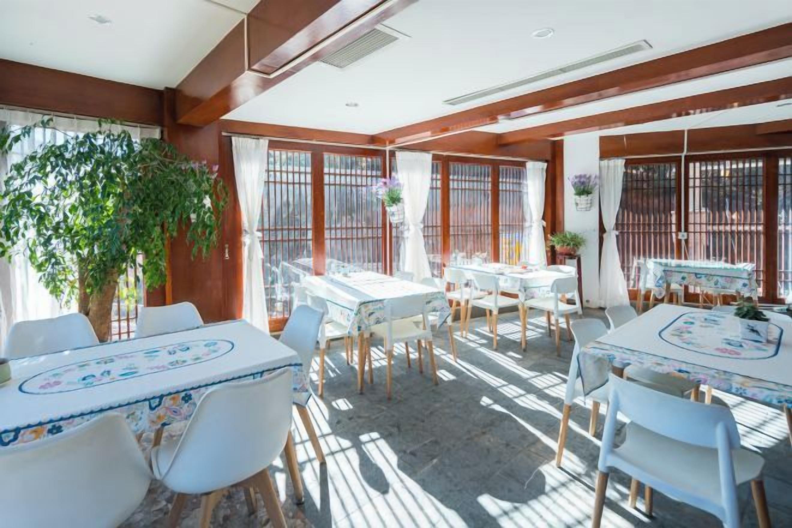 A dining area with tables and chairs, large windows, and a plant.