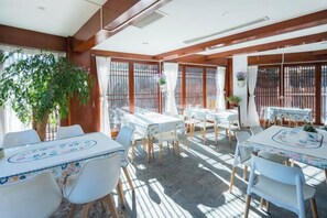 A dining area with tables and chairs, large windows, and a plant. - YingHuoChong (Ninglang)