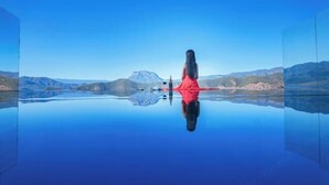 A person in a red dress standing on a reflective surface with a mountainous landscape in the background.