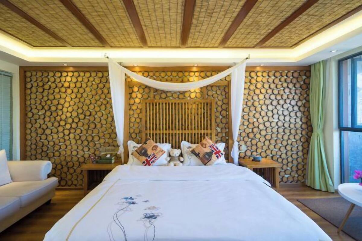 Quarto com cama de dossel, parede de madeira com padrões circulares, sofá e mesa com vista para o exterior.