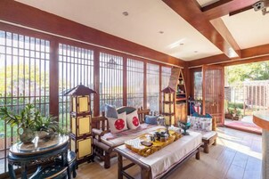Una habitación tradicional japonesa con suelo de tatami, una mesa baja con una bandeja de comida y vistas a un jardín a través de celosías shoji.