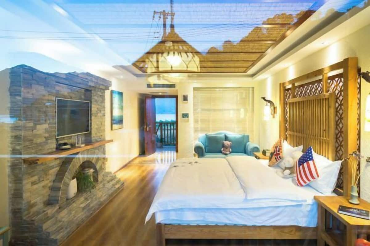Quarto com parede de pedra, cama com roupa de cama branca, televisão e vista para o exterior.