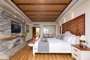 A bedroom with a stone fireplace, a bed with a headboard, a bedside table, and a nightstand.
