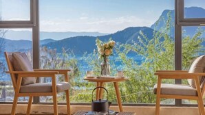 A room with two wooden chairs, a small table with a vase of flowers, and a tray with teapots.