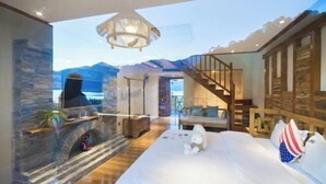 A bedroom with a large bed, a fireplace, a view of mountains, and a wooden staircase.