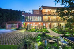 Un edificio de dos plantas con un balcón en el piso superior, una entrada bien iluminada y un jardín ajardinado.