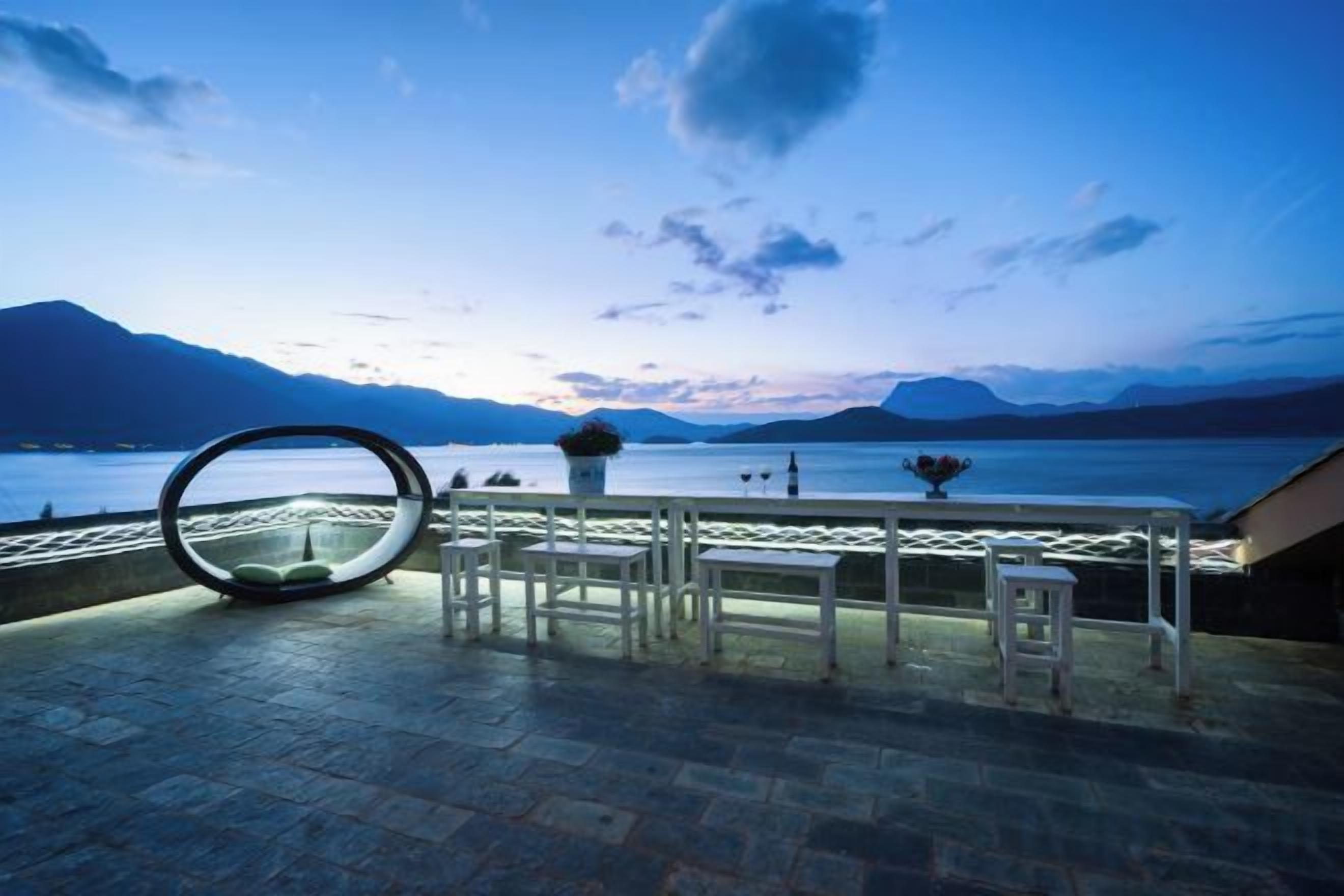 Een terras met een tafel en stoelen, met uitzicht op water en bergen.