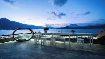 Een terras met een tafel en stoelen, met uitzicht op water en bergen.