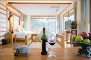 Quarto de hotel com uma cama, uma mesa de jantar com uma garrafa de vinho e um copo, e uma tigela de frutas.