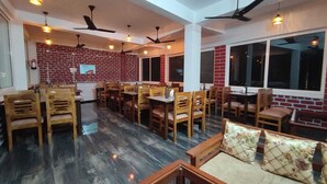 A spacious dining area with wooden furniture, a brick wall, and large windows. - Hotel StudioZ Sahastradhara (Dehradun)