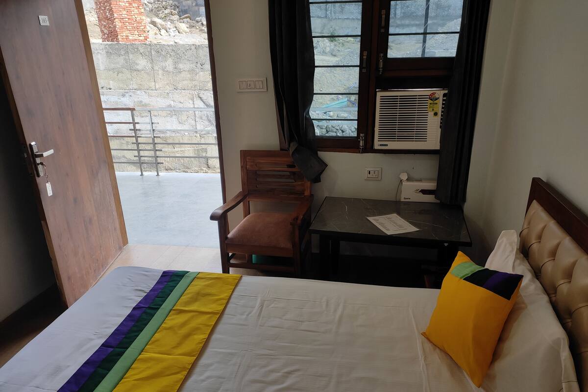 Une chambre d’hôtel équipée d’un lit, d’un bureau, d’une chaise et d’une fenêtre avec un climatiseur.