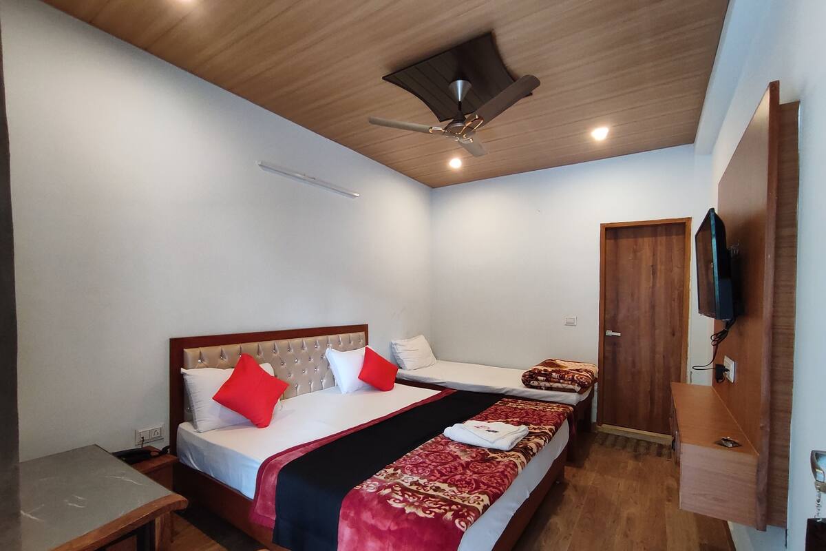 Une chambre d’hôtel avec deux lits, un plafond en bois, un téléviseur fixé au mur et un bureau.