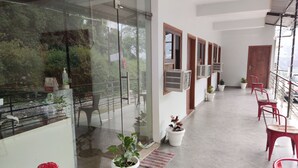 A reception area with a glass wall, potted plants, and red chairs. - Hotel StudioZ Sahastradhara (Dehradun)