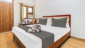 A neatly made bed with a tray of breakfast items, a wooden door, a window with curtains, and a small table with a vase of flowers. - Hotel StudioZ Sahastradhara (Dehradun)