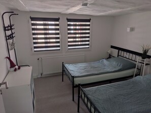 Une chambre avec deux lits, un radiateur, un bureau et une fenêtre avec des stores.