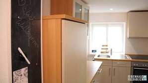 A modern kitchen with wooden cabinets, a built-in oven, and a window providing natural light. - Ferienhaus Fuldablick Das Ferienhaus Inmitten der Altstadt von Rotenburg /fulda (Rotenburg an der Fulda)
