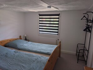 A room with two wooden beds, a radiator, a window with blinds, and a black metal rack with hangers.
