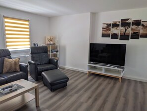 Un salon moderne avec un canapé en cuir, un pouf et un téléviseur à écran plat posé sur un meuble en bois.