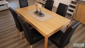 A dining area with a wooden table, black chairs, and a TV in the background. - Ferienhaus Fuldablick Das Ferienhaus Inmitten der Altstadt von Rotenburg /fulda (Rotenburg an der Fulda)