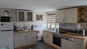 A compact kitchen with a microwave, coffee maker, and a sink. There is a fire extinguisher and a window with blinds.
