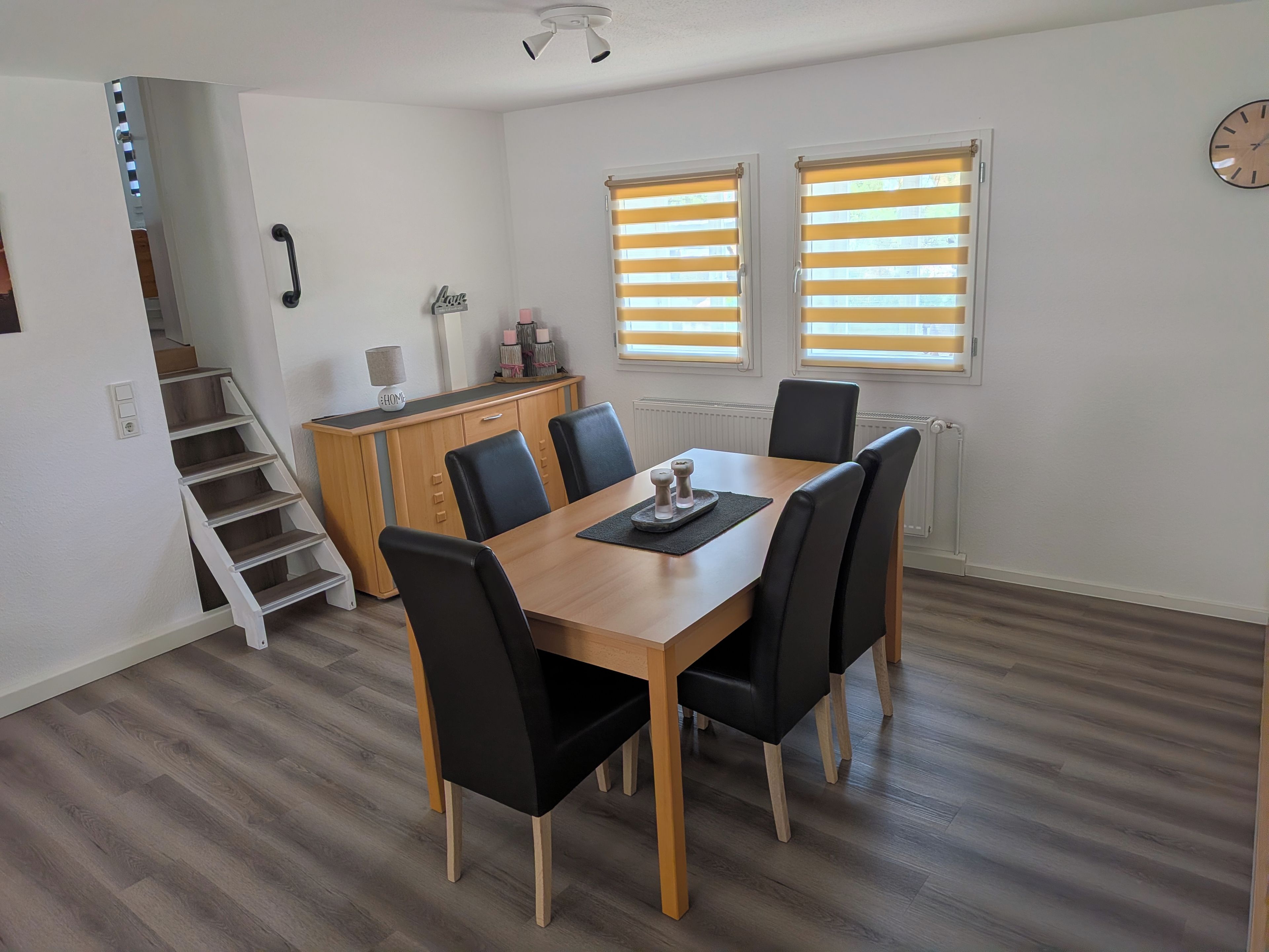 Ein Essbereich mit einem Holztisch, schwarzen Stühlen und einer Treppe, die zu einer oberen Ebene führt.