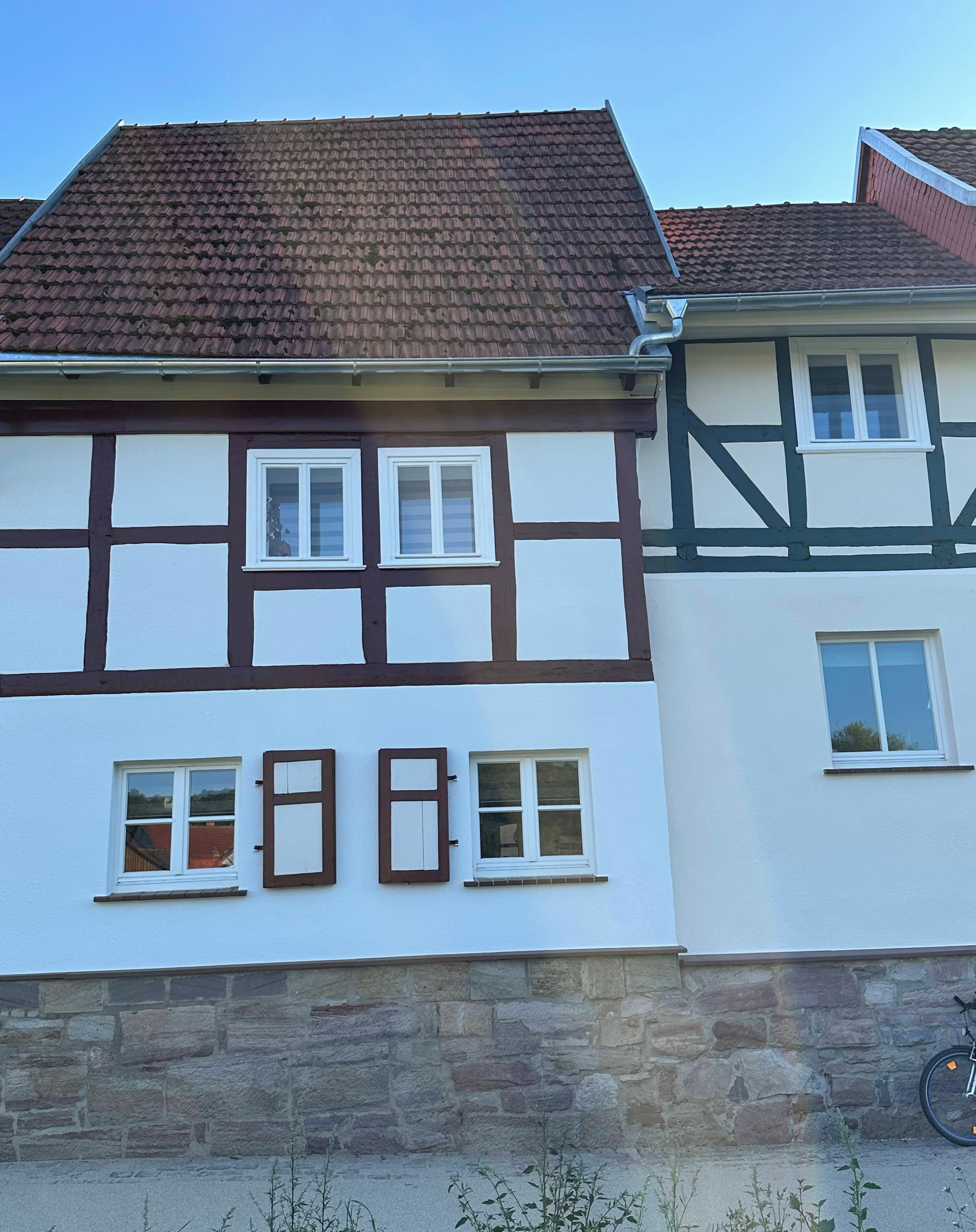 A traditional half-timbered house with a stone foundation, multiple windows, and a tiled roof.