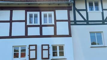 A traditional half-timbered house with a stone foundation, multiple windows, and a tiled roof.