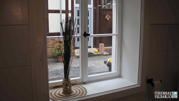 A window with a view of a garden, a door, and a brick wall. - Ferienhaus Fuldablick Das Ferienhaus Inmitten der Altstadt von Rotenburg /fulda (Rotenburg an der Fulda)
